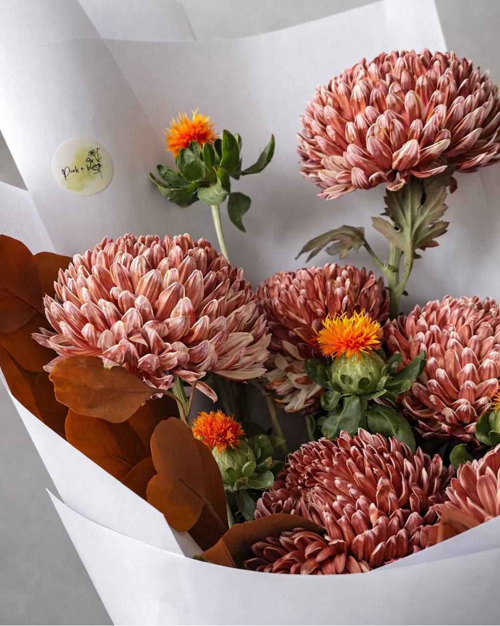 Bouquet of pink and orange flowers in a white wrap on a light gray background