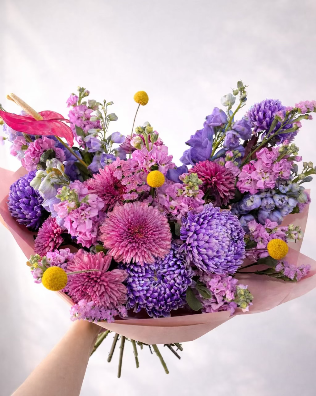 Bouquet of colorful flowers held by a hand on a light background