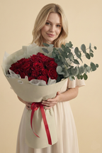 Woman holding a bouquet of red roses with greenery against a beige background