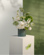 Floral arrangement in a green vase on a white pedestal with a light green background